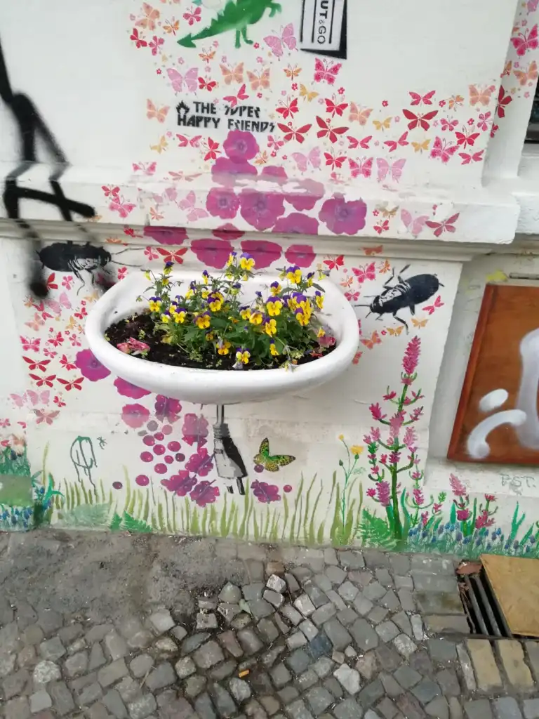 Waschbecken, mit Blumen bepflanzt, vor einer bemalten Hauswand 